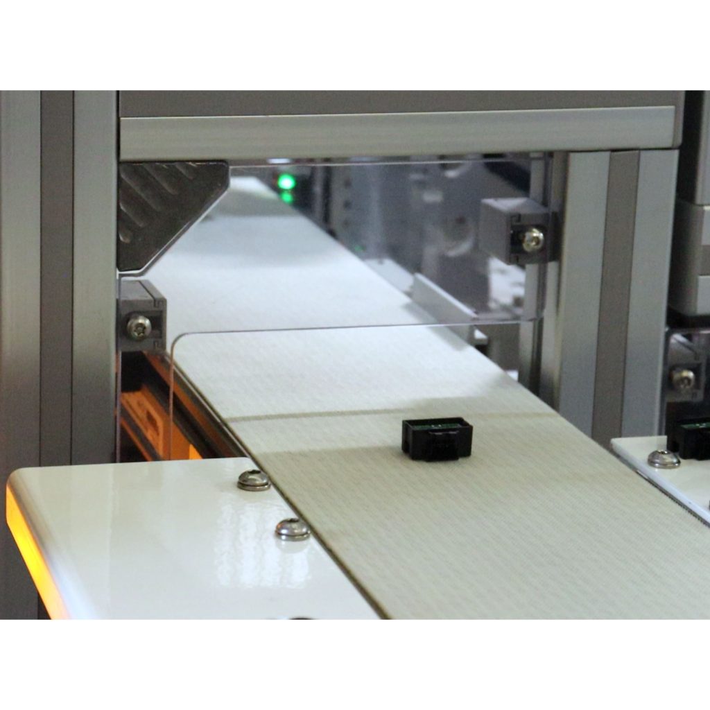 Completed automotive electronics exiting automated assembly system on final conveyor